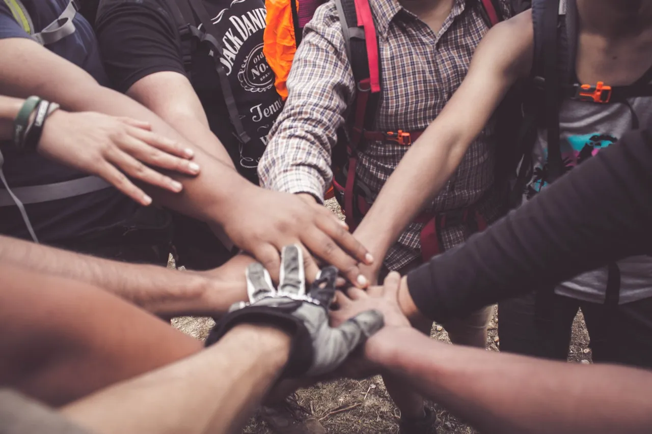 Group of people with backpacks stacking hands together in a team huddle